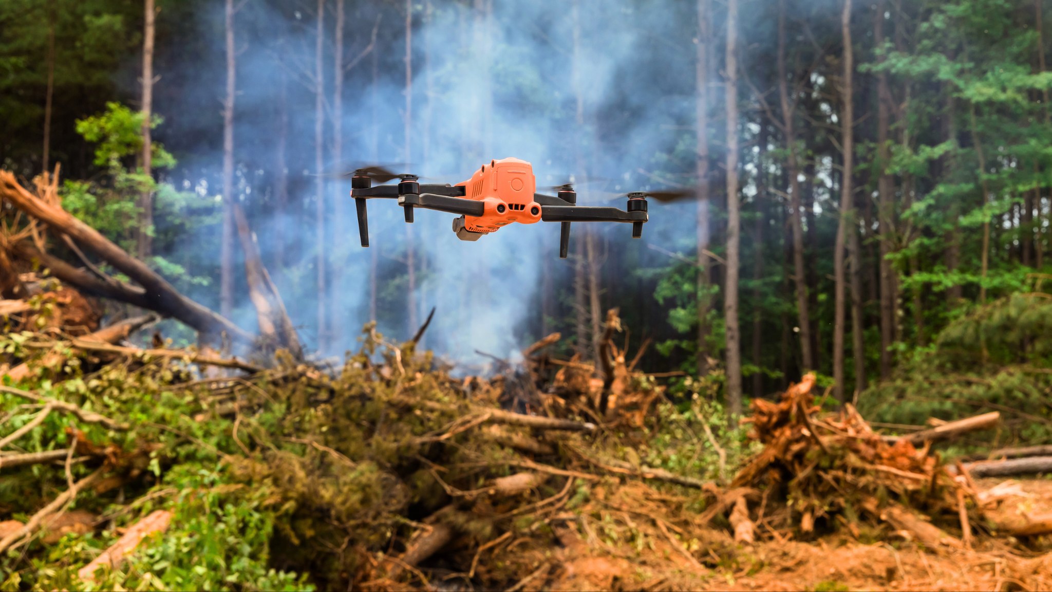 Orange drone operating over a smoky woodland scene